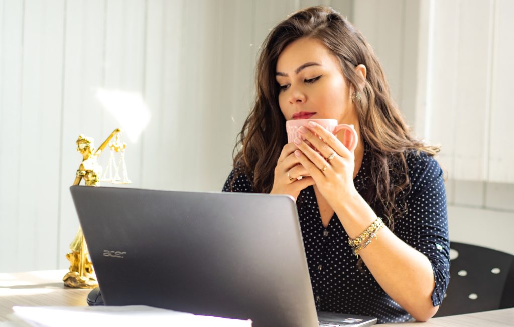 Mujer mirando su computador mientras sostiene una taza en sus manos
