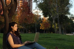 Mujer sentada en parque con computadora sobre las piernas