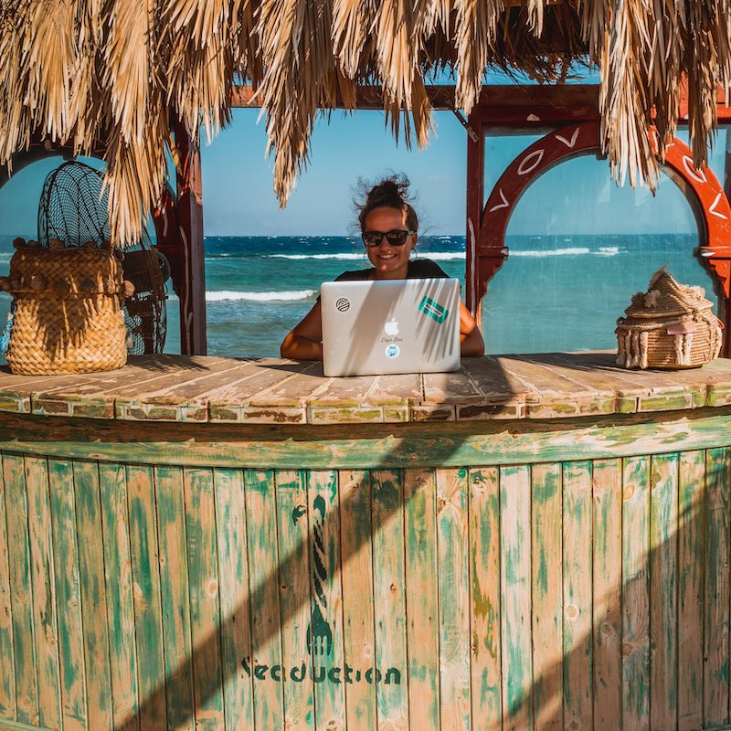Mujer sonriente trabajando en su computadora sobre un bar en un choza en el caribe