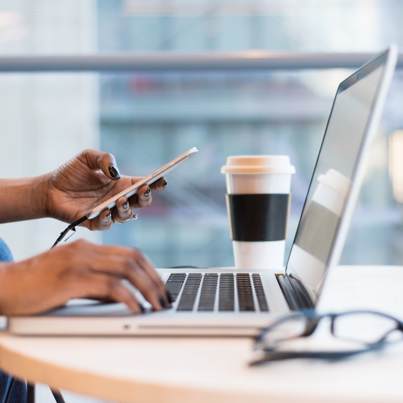 Mujer con uñas de color negro sosteniendo un teléfono con la mano izquierda y tecleando en su computadora con la derecha