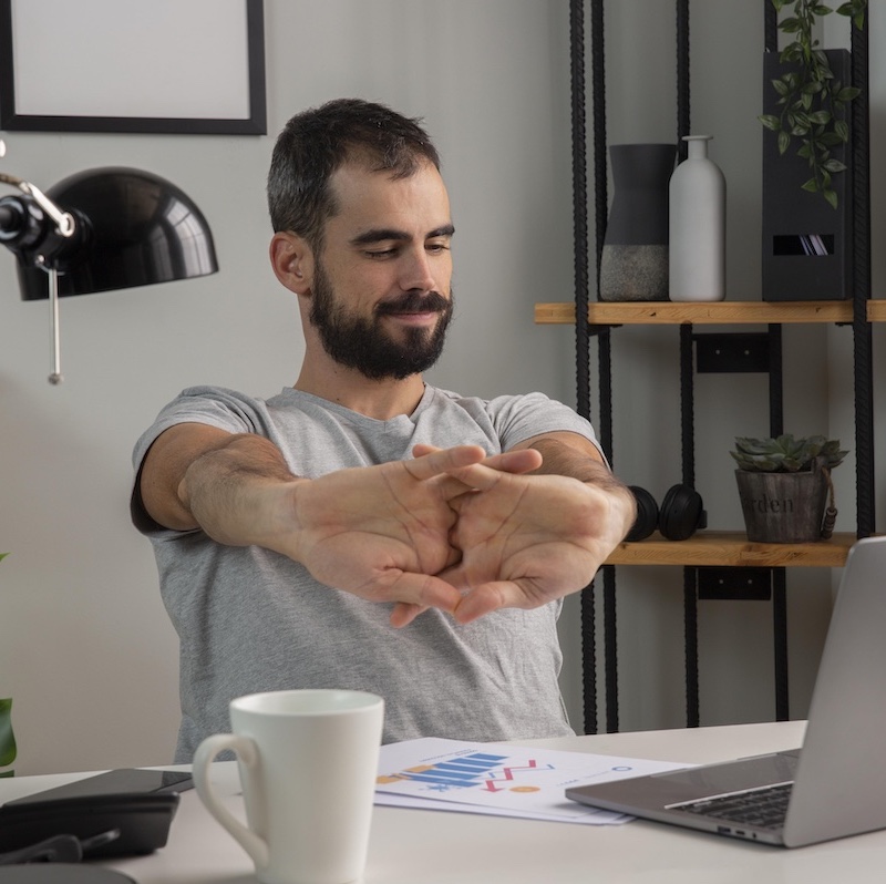 Trabajador remoto estirándose mientras ve la pantalla de su computadora