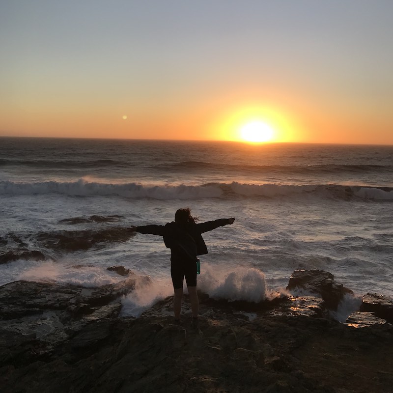 Mujer con brazos extendidos frente al mar al atardecer