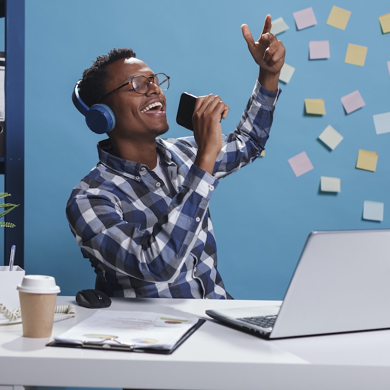 Freelancer distraído cantando con su teléfono frente a su ordenador