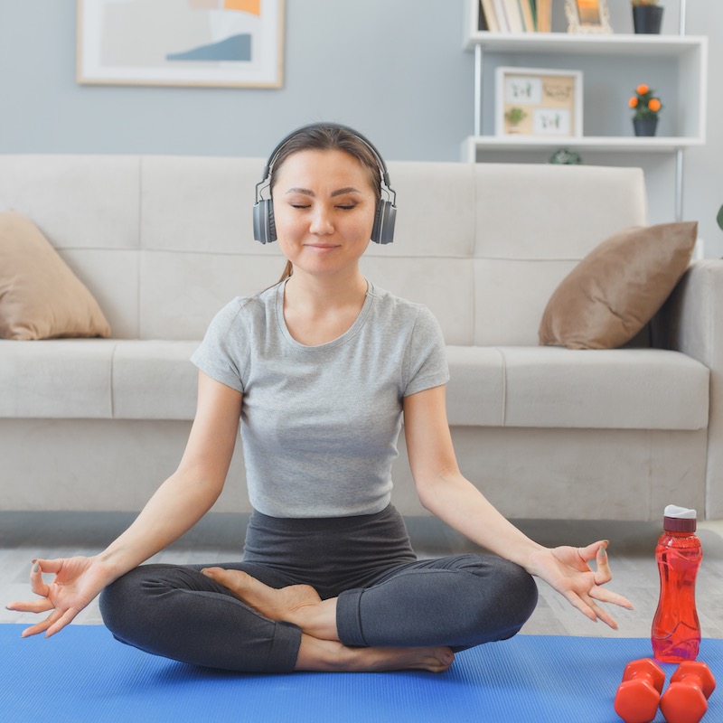 Mujer meditando en la sala de su casa con audífonos