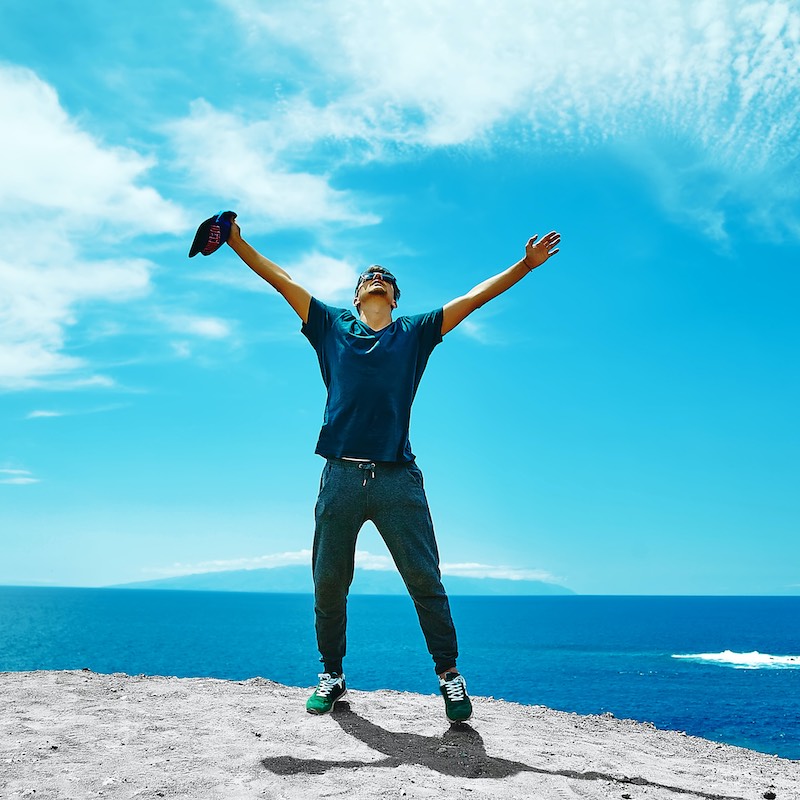 hombre feliz con brazos extendidos en una roca frente al mar.