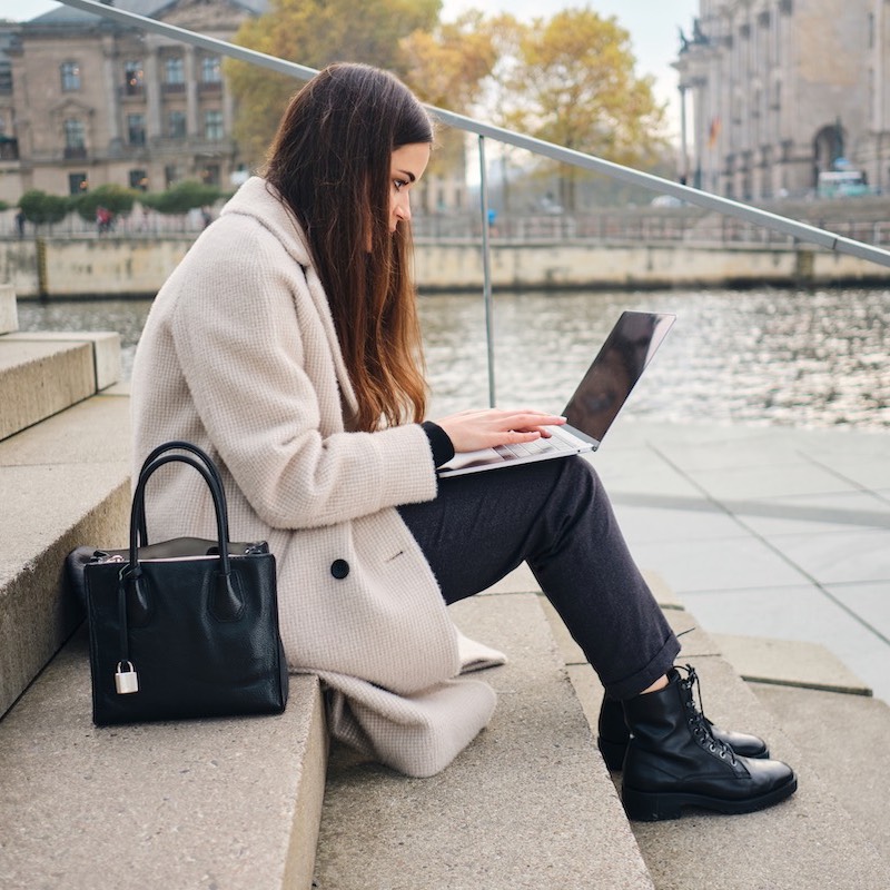 Una freelancer sentada en una escalera con su computadora junto a un canal en la ciudad. Saber cuánto gana un freelancer es complicado, pero un nuevo estudio revela que los Europeos generan mayores ingresos.
