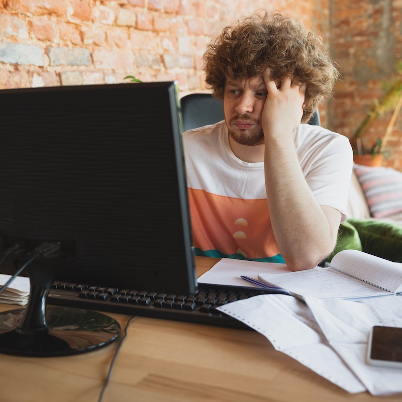 Hombre frente a computador y cuadernos con cara de frustración 