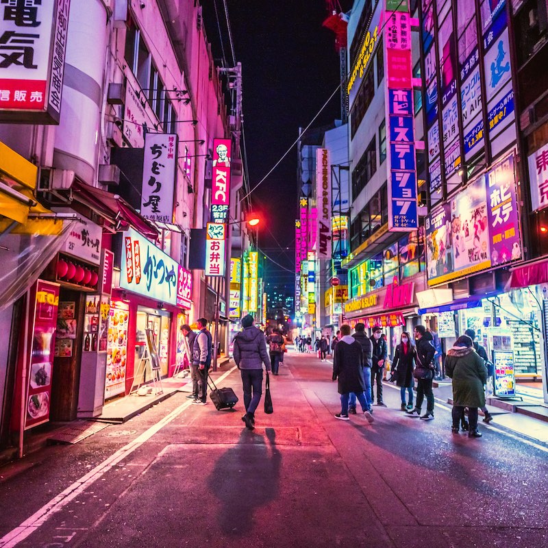 Calle de Tokio iluminada con carteles comerciales en la noche. Transeúntes con abrigo caminando y recorriendo las tiendas.